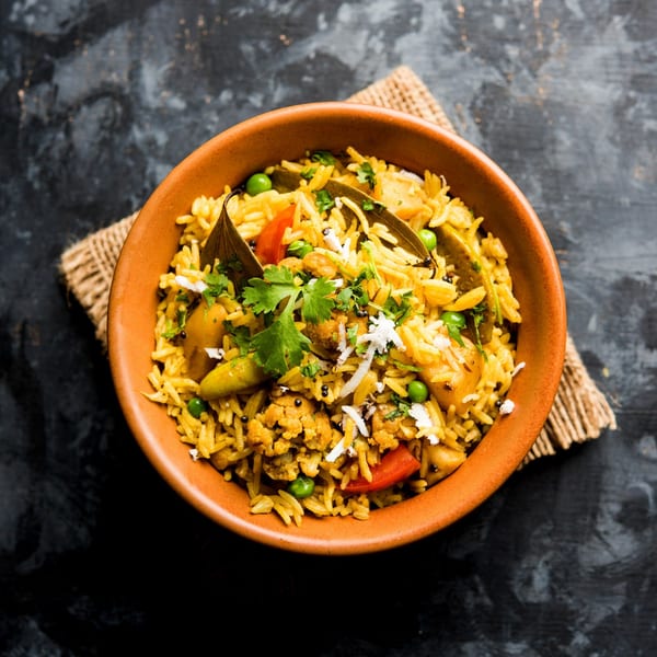 A terracotta bowl of Brindavan Cafe's Indian vegetable pulao, garnished with cilantro and coconut.