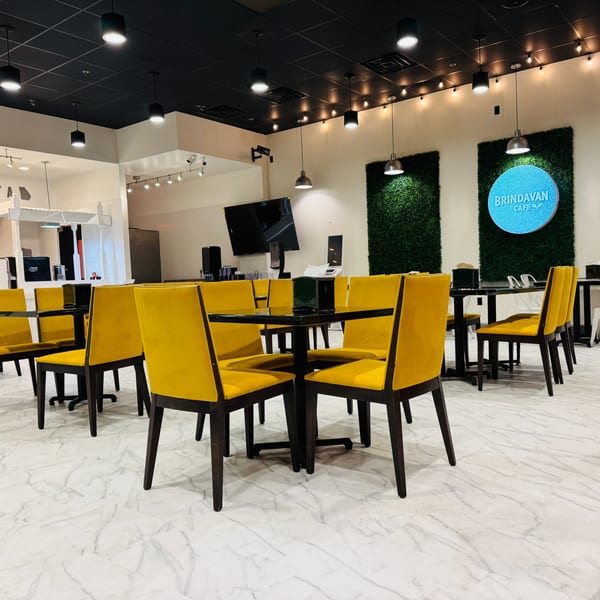 Modern Brindavan Cafe interior with yellow chairs, dark tables, and green wall accents under bright lighting.