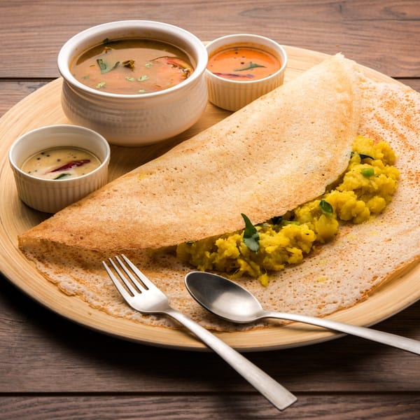 Masala dosa with potato filling, served with sambar, coconut chutney, and tomato chutney on a wooden plate.