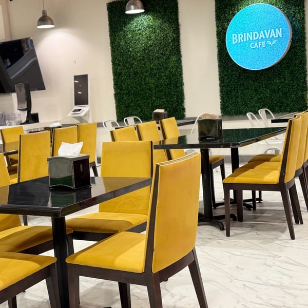 Interior of Brindavan Cafe with yellow chairs, black tables, and a green wall with the cafe's blue logo.