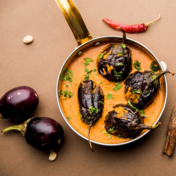 Brindavan Cafe's Indian eggplant curry, Bagara Baingan, in a golden pan with whole eggplants and spices.