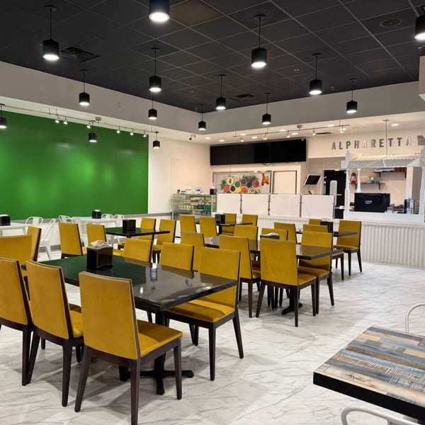 Modern Indian restaurant interior with yellow chairs, black tables, a green accent wall, and a serving counter.